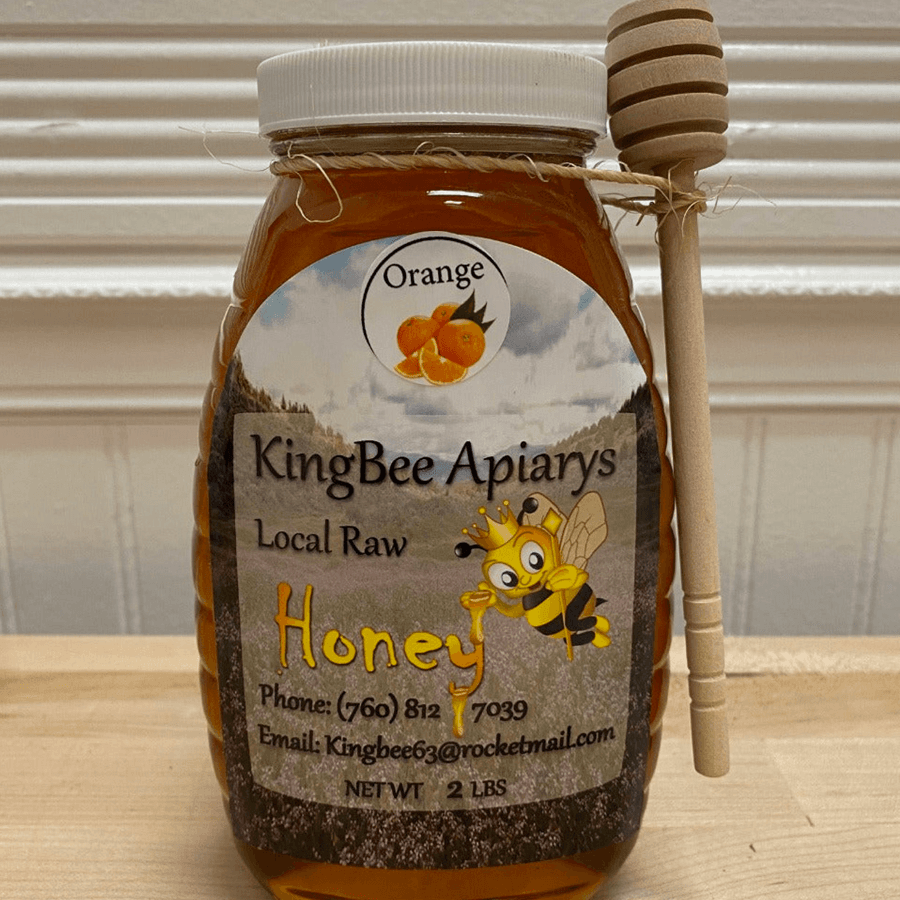 A jar of local raw orange honey with a wooden dipper attached.